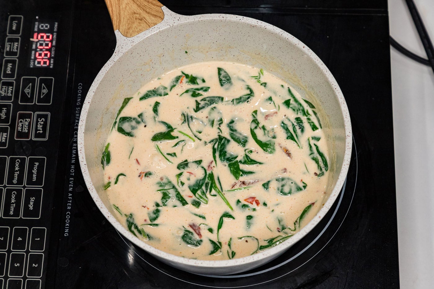 spinach added to cream sauce in a skillet with sun dried tomatoes