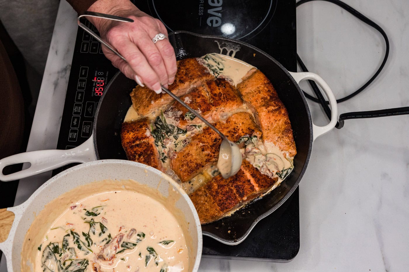 spooning cream sauce over salmon in a skillet