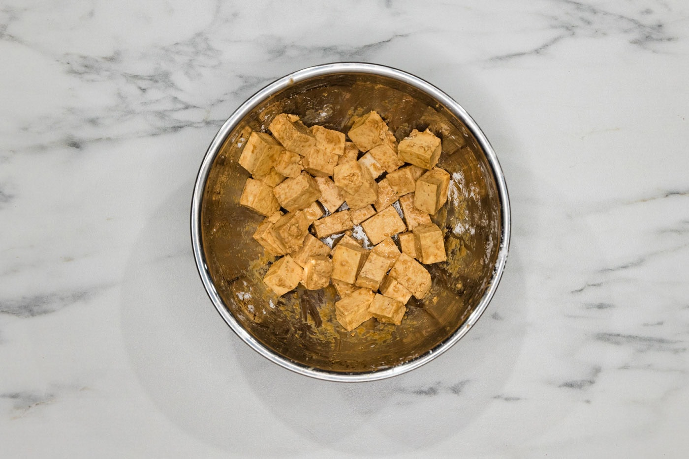 tofu cubes tossed in cornstarch and seasonings in a mixing bowl