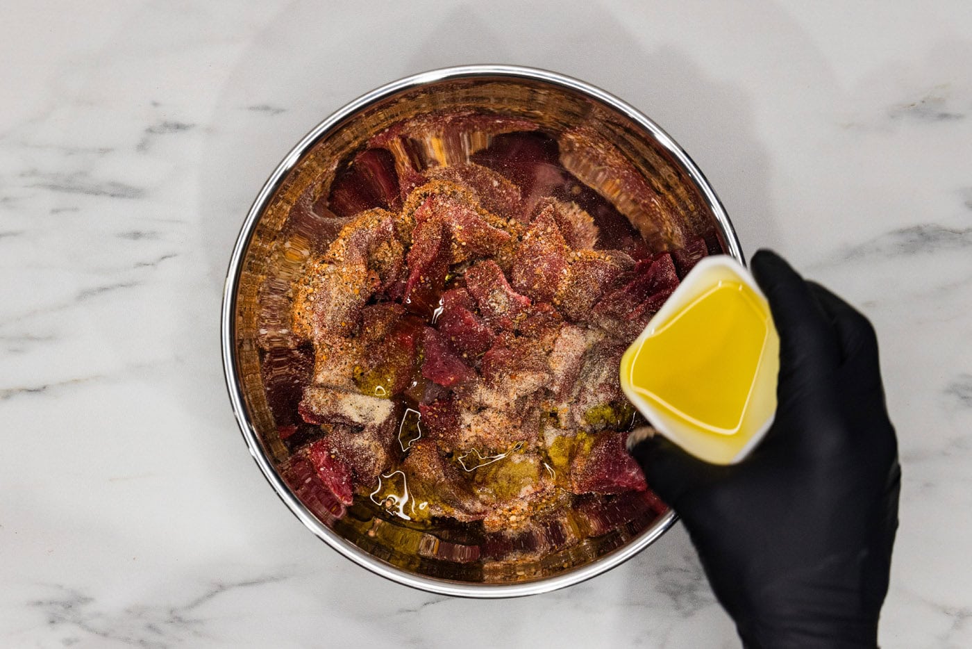 pouring olive oil into bowl of cubed steak and seasonings