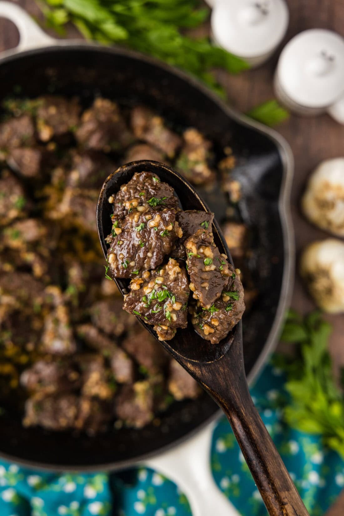 Spoonful of Garlic Butter Steak Bites held above a skillet of Garlic Butter Steak Bites