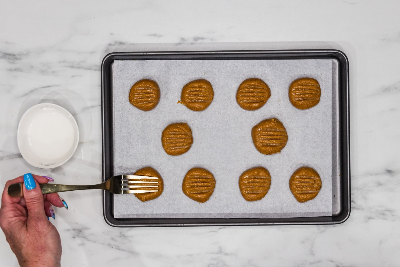 fork pressing into peanut butter cookie dough on a baking sheet