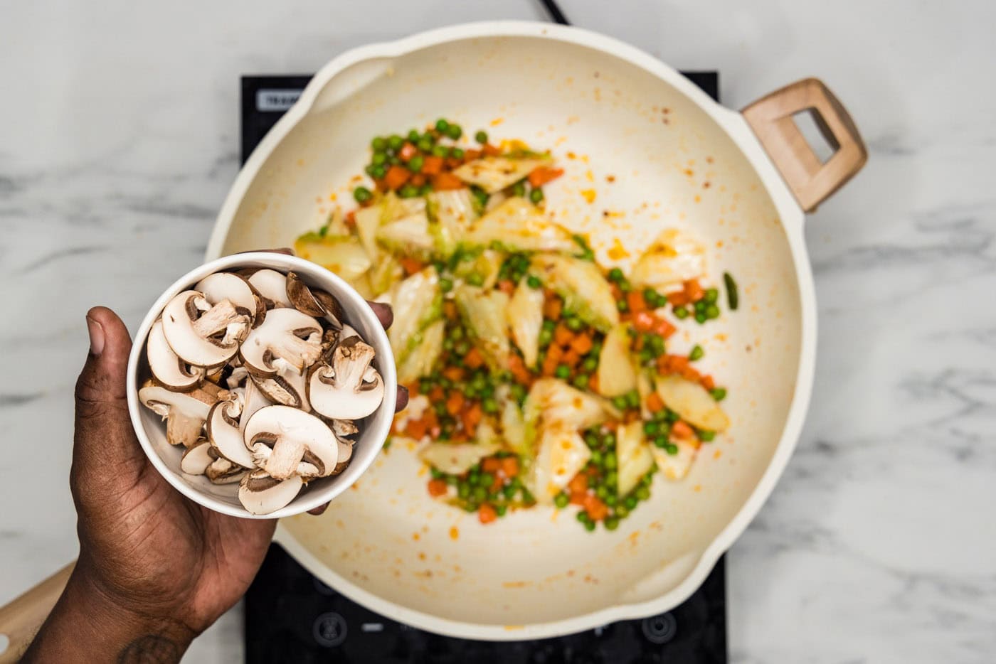 adding mushrooms to stir fried veggies in a skillet