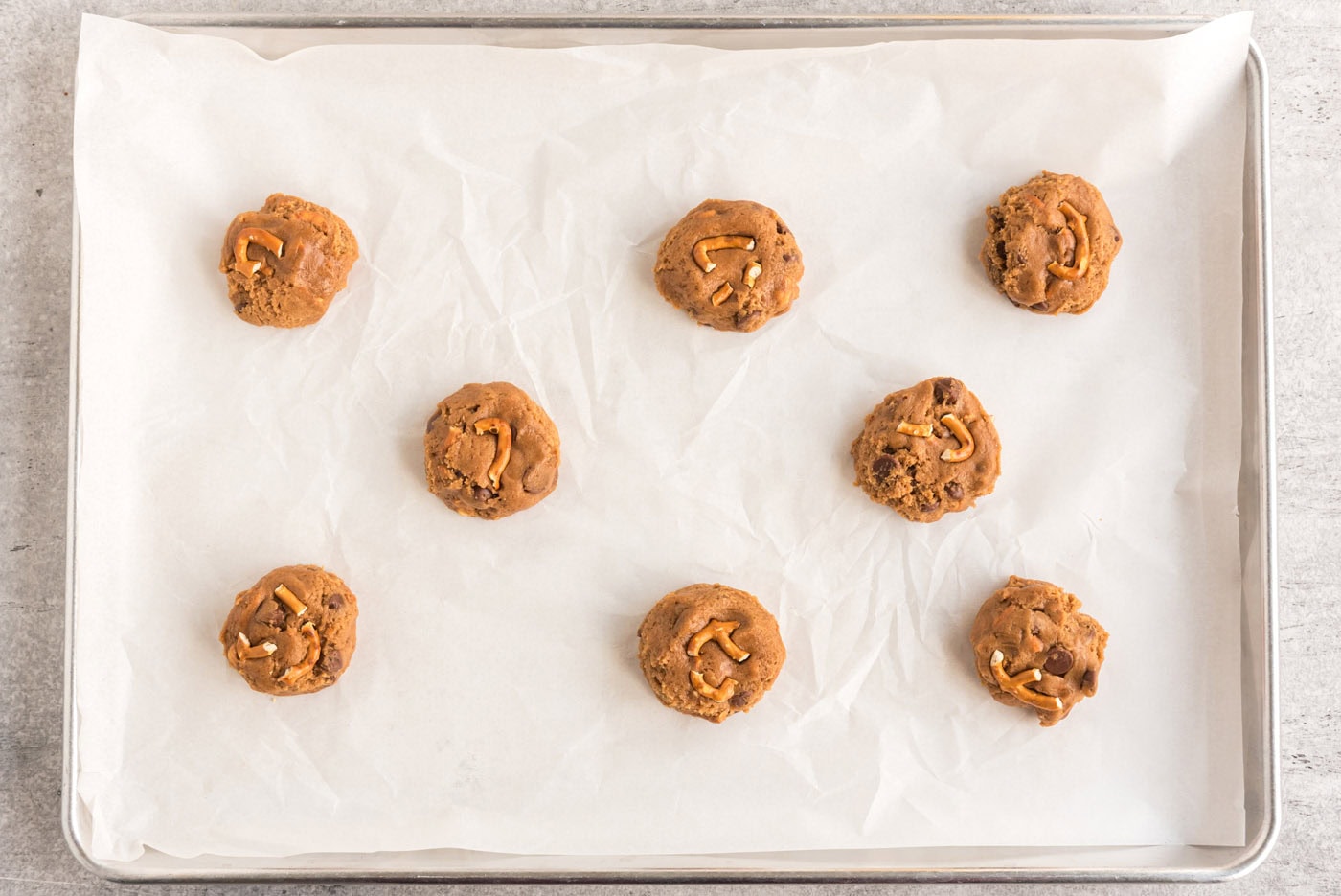 cookie dough balls with pretzels on a baking sheet