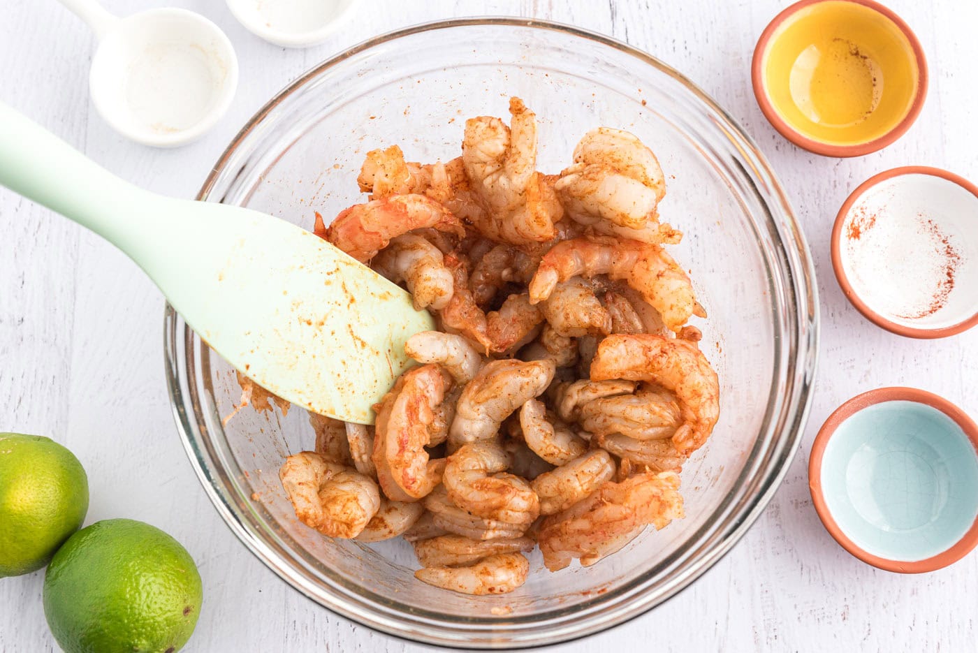 seasoned raw shrimp in a bowl with a rubber spatula