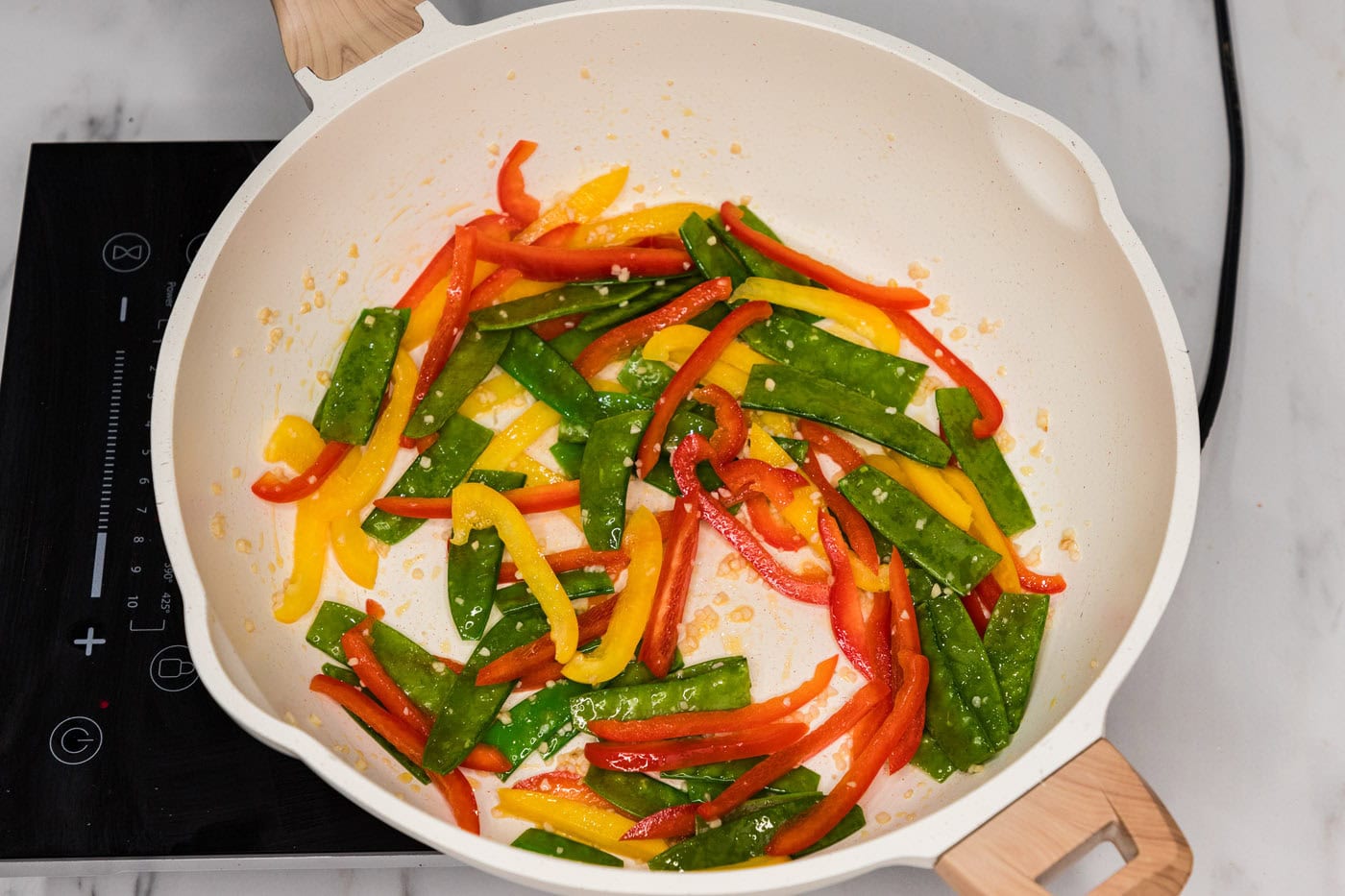 sliced bell peppers and snow peas in a skillet with oil