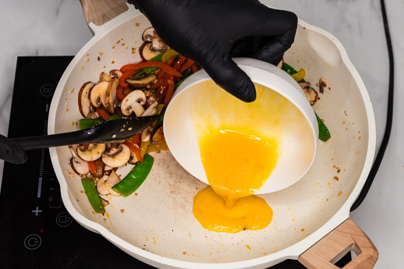 pouring egg into skillet with vegetables