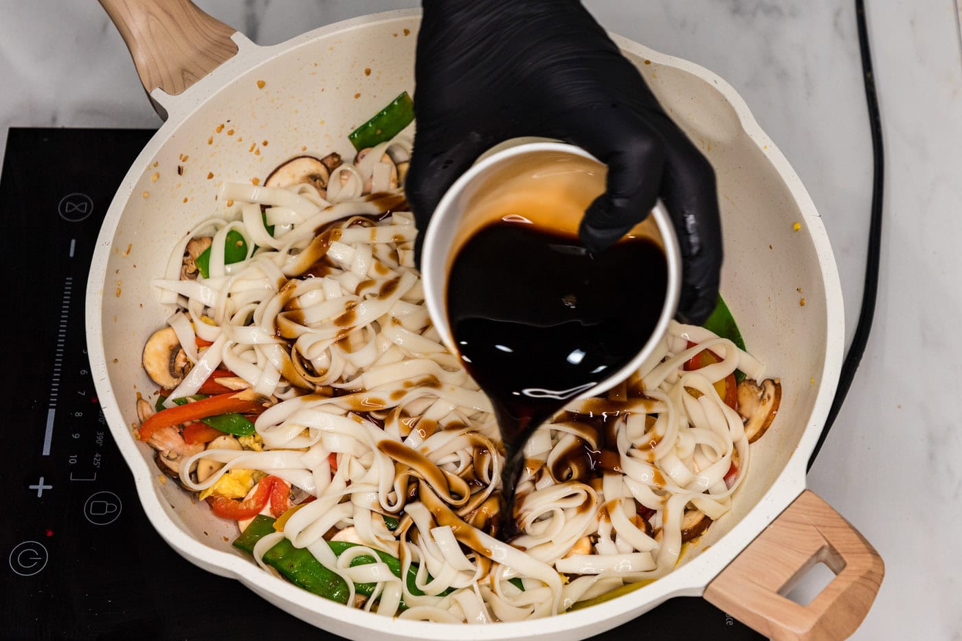 pouring sauce into skillet with vegetable lo mein