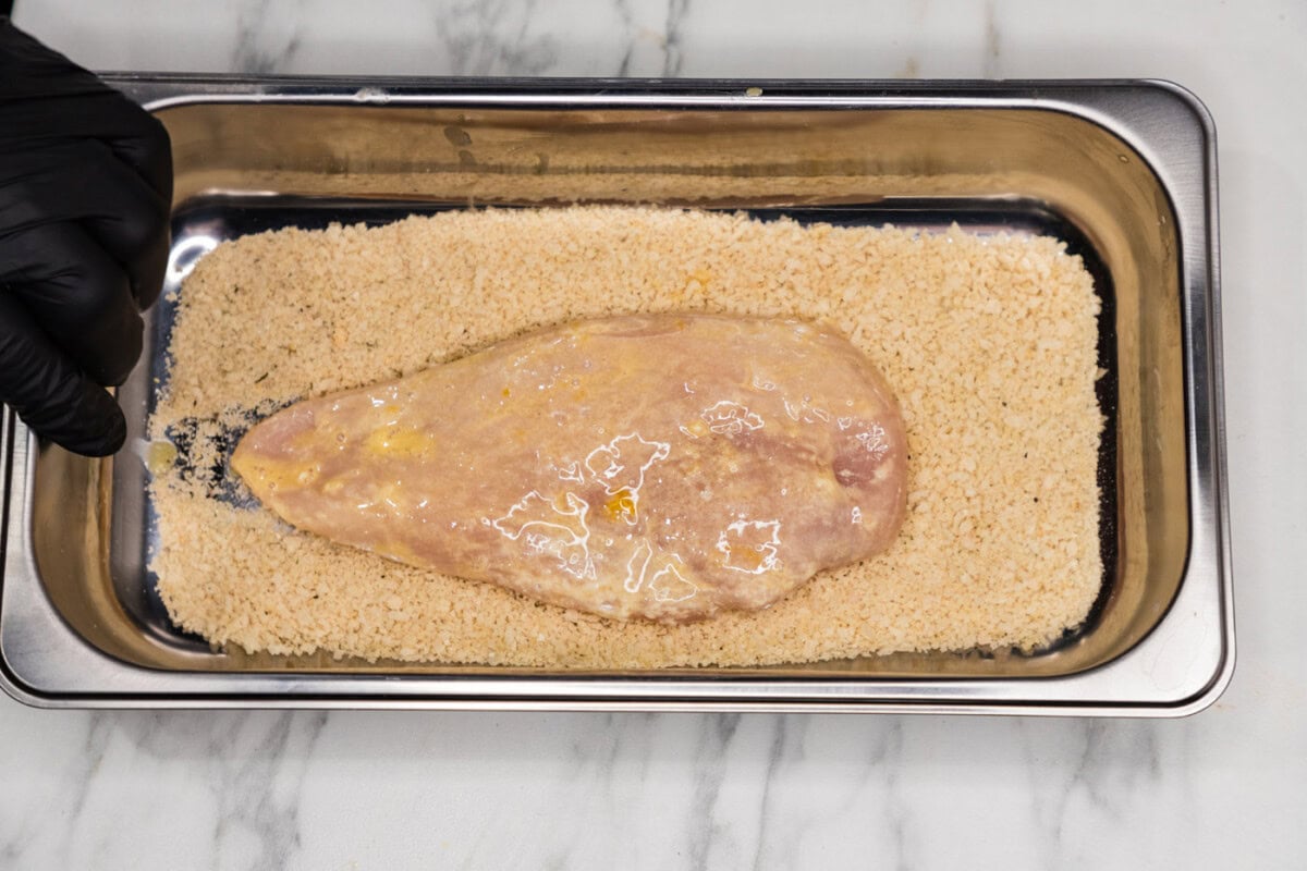 dredged chicken breast in a pan with panko breadcrumbs