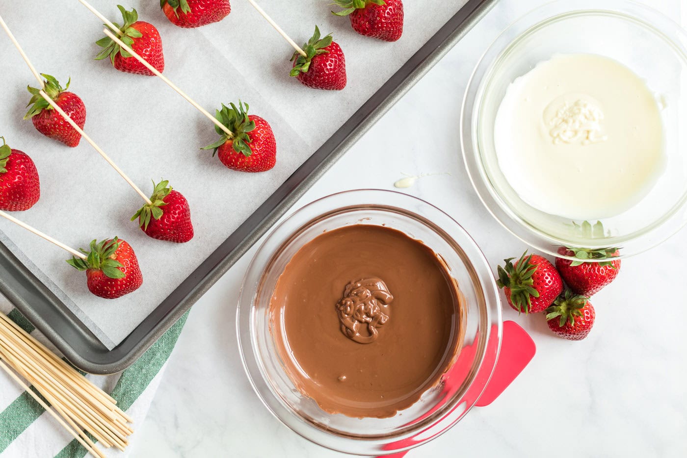 strawberries skewered on a pan and a bowl of melted chocolate