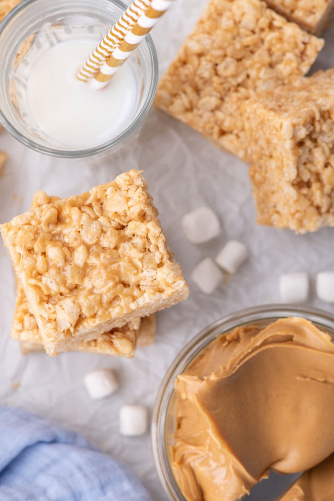 Stacked Peanut Butter Rice Krispie Treats with a bowl of peanut butter and a glass of milk to the side