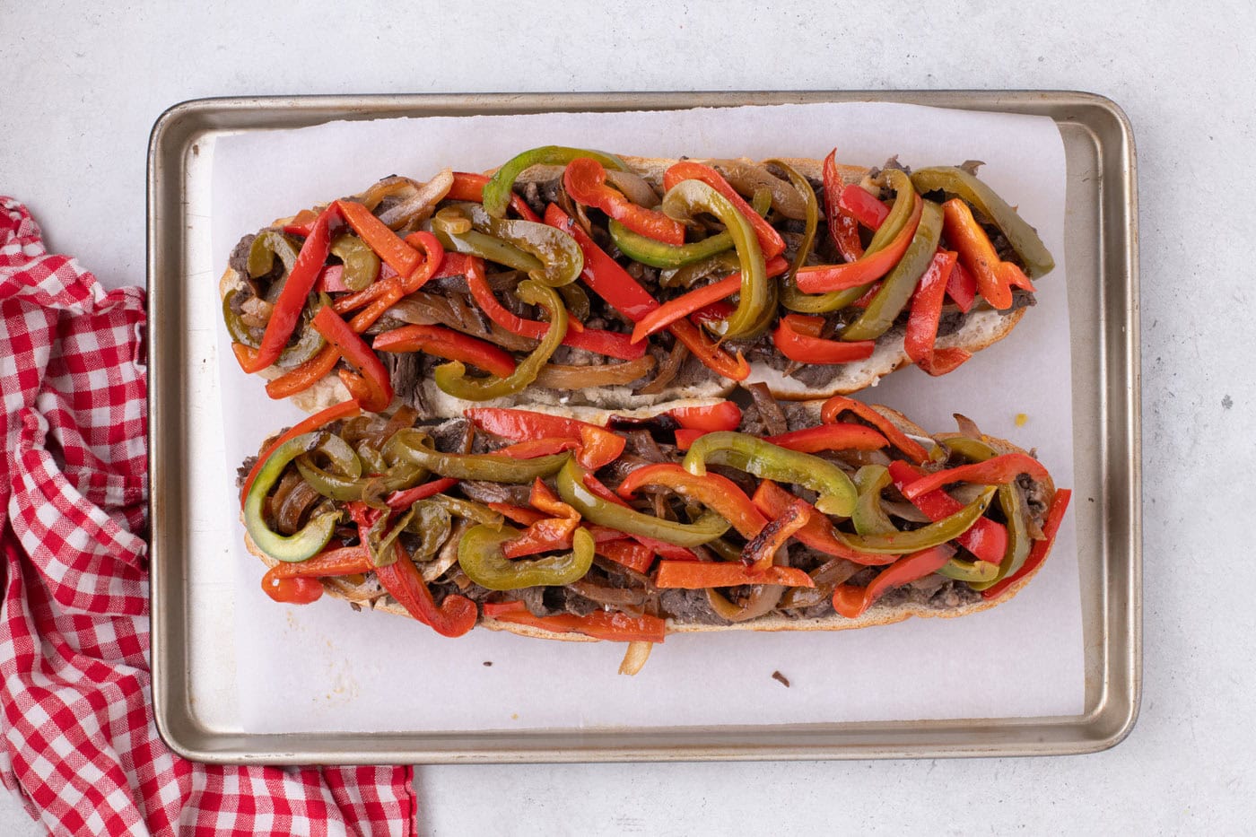 loaf of bread topped with steak, onions, and bell peppers