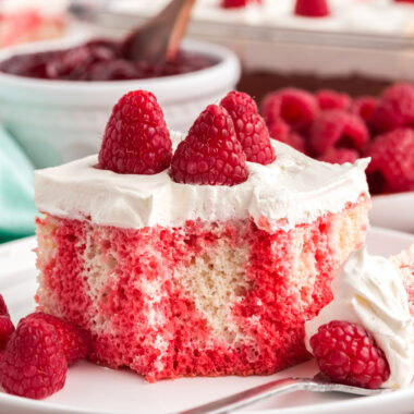 Close up photo of Raspberry Poke Cake on a plate with a bite removed