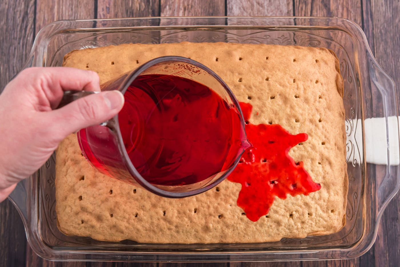 pouring raspberry jello over cake