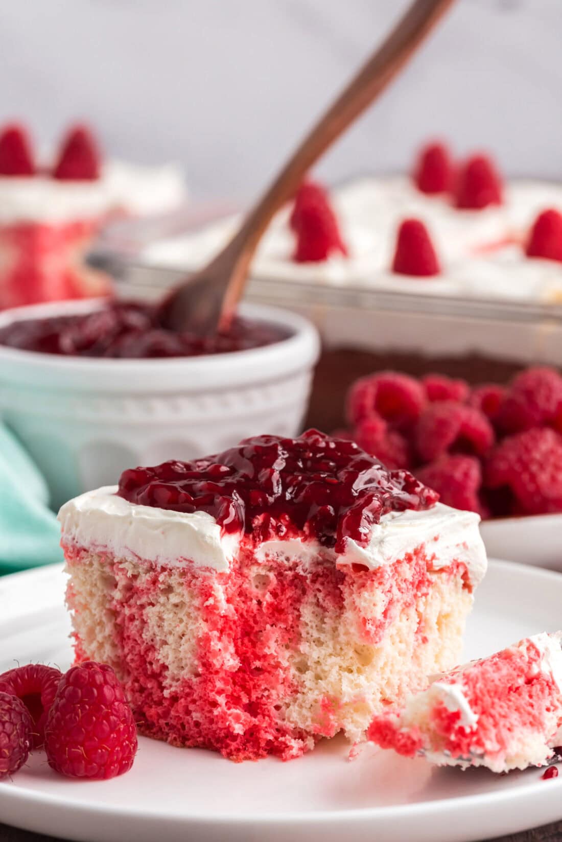 Slice of Raspberry Poke Cake on a plate with a bite removed