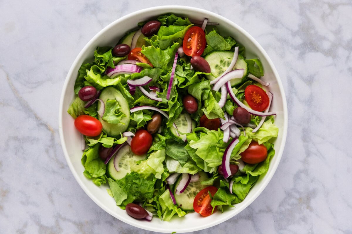 lettuce in a bowl with tomatoes, olives, cucumbers, and red onion