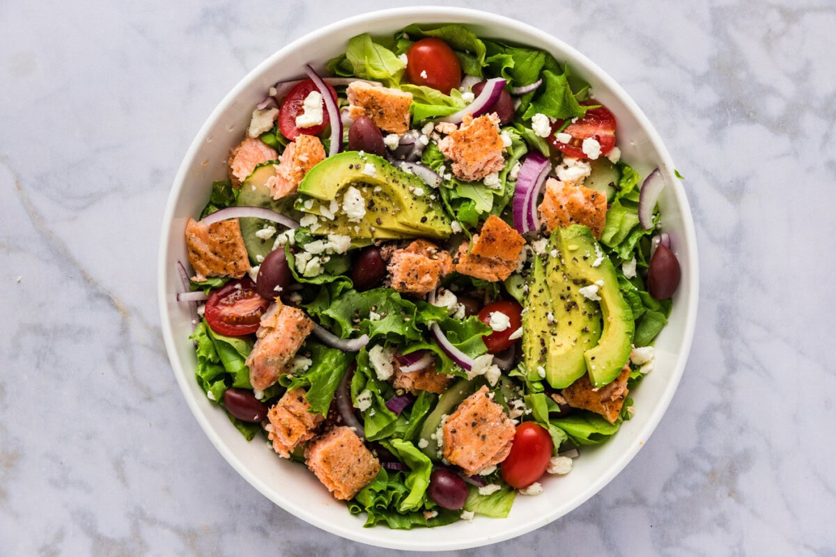 avocado, feta, and salmon added to salad in a bowl