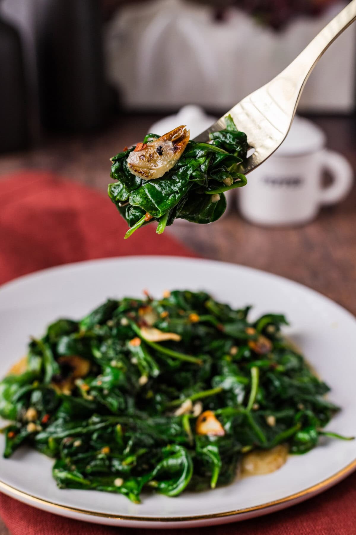 Fork of Stir Fried Spinach held above a plate of Stir Fried Spinach