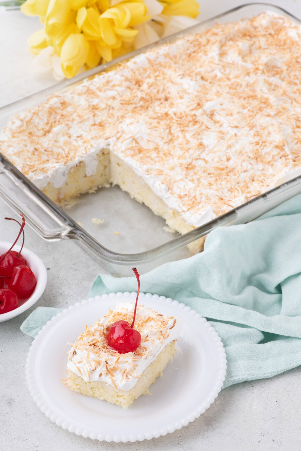Slice of Coconut Poke Cake on a plate with the rest of the cake in the background