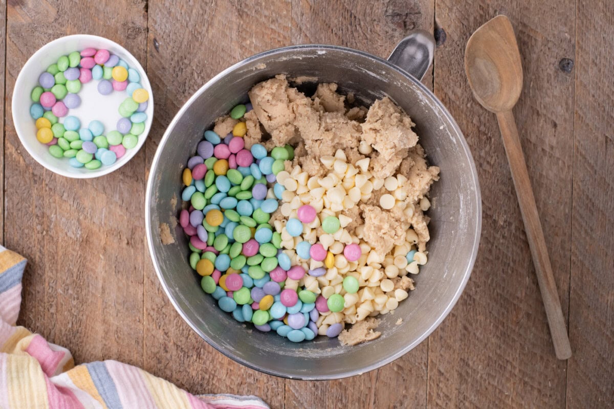 white chocolate chips and M&Ms added to cookie dough in a bowl