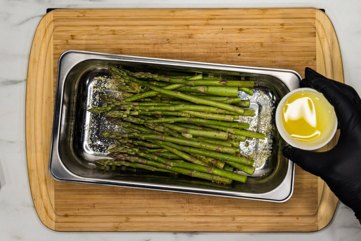 hand holding olive oil in a bowl over asparagus