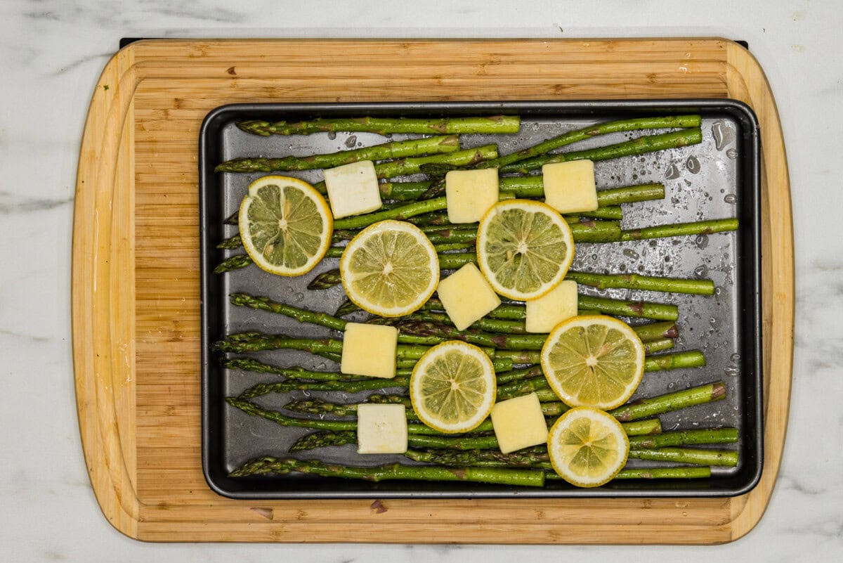 asparagus on a pan with butter pats and lemon slices