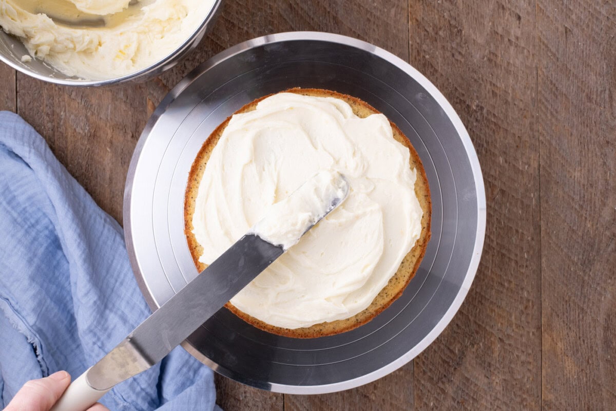 icing spatula spreading lemon cream cheese frosting on cake