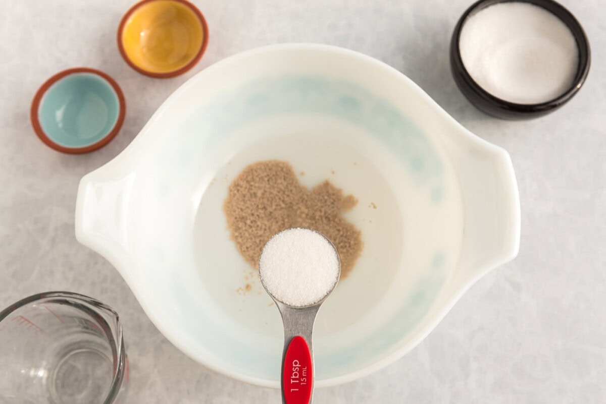 adding sugar to bowl of yeast and warm water