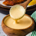 Close up photo of a spoon drizzling Remoulade Sauce into a bowl