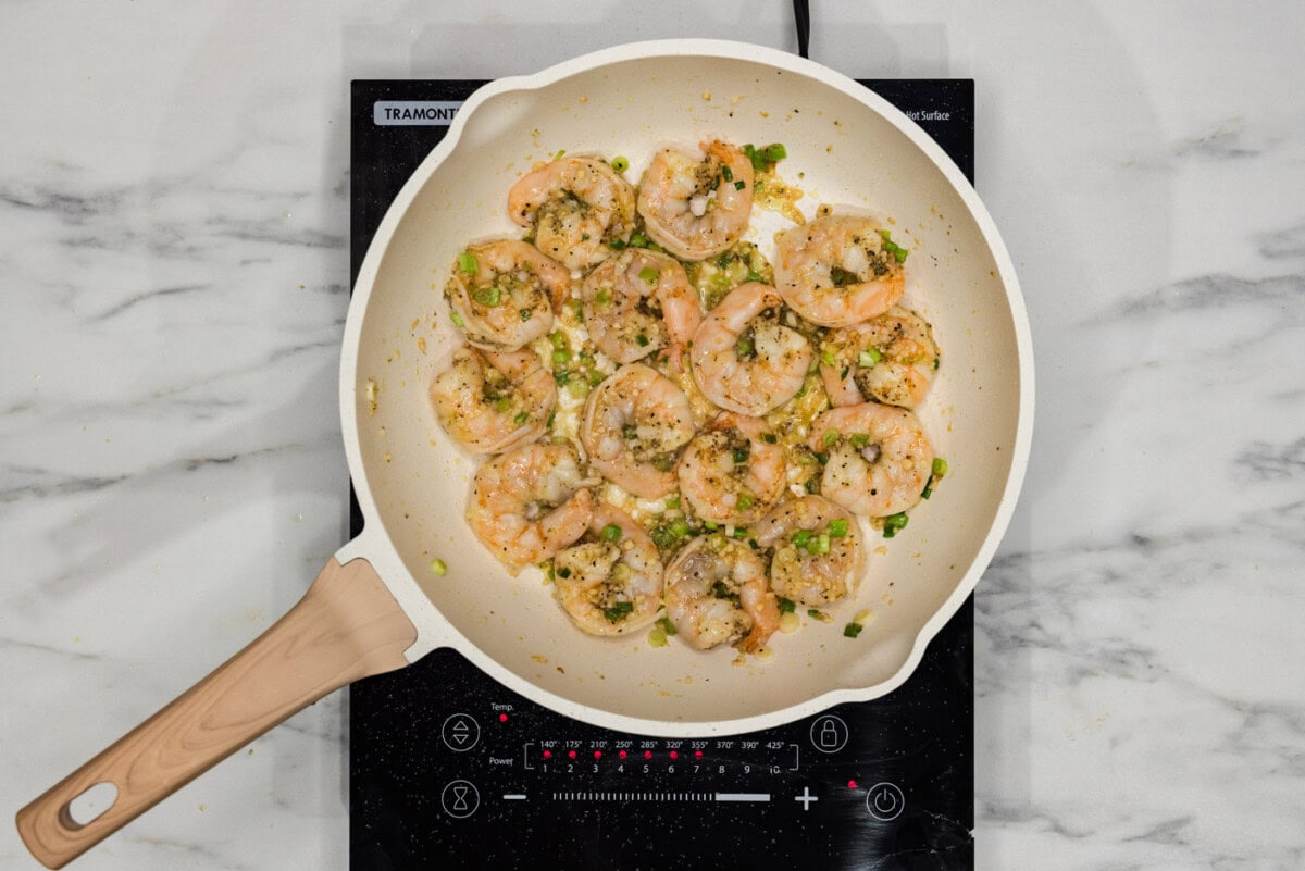 pink cooked shrimp in skillet with green onions