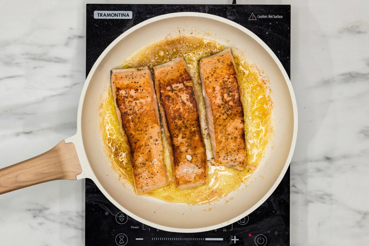salmon filets cooking in a skillet with oil and butter