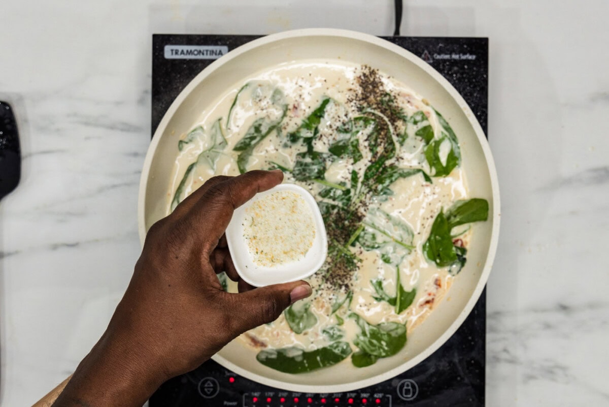 adding garlic salt to cream sauce with spinach in a skillet