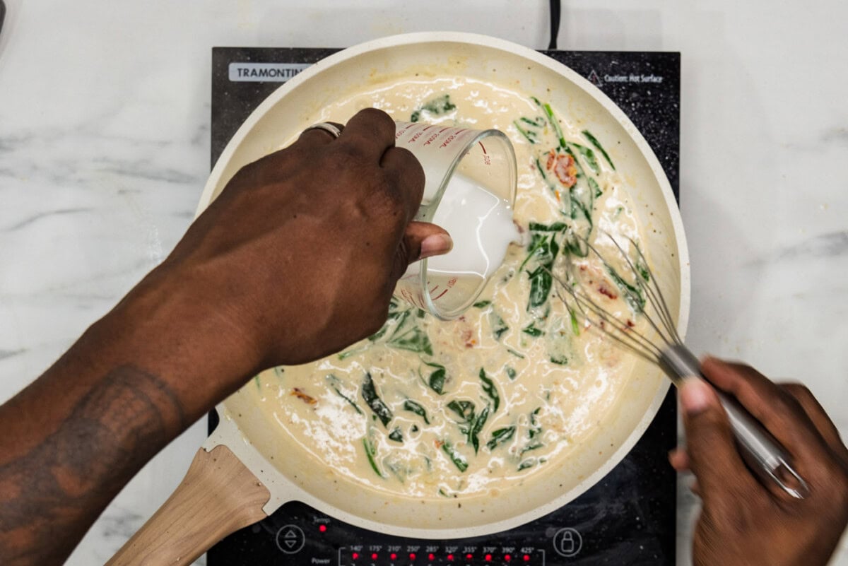 pouring cornstarch slurry into skillet with cream sauce