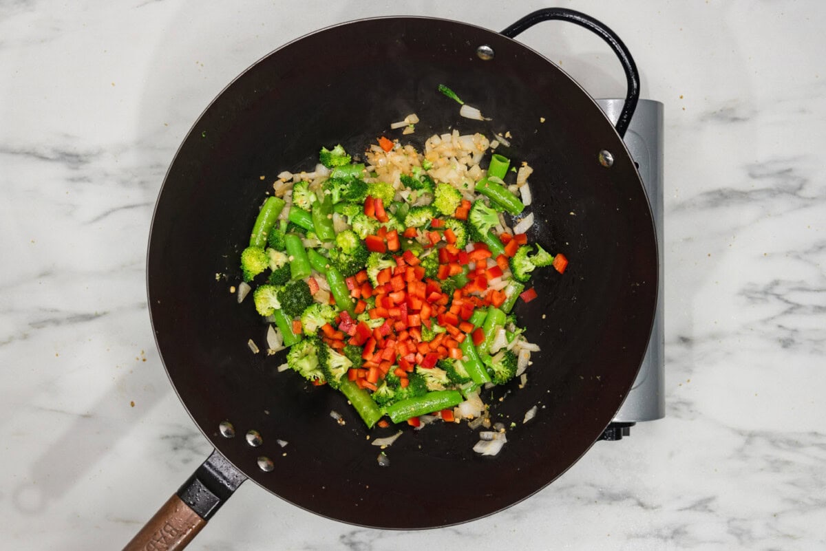 Onion, snap peas, broccoli, and red bell pepper in a wok