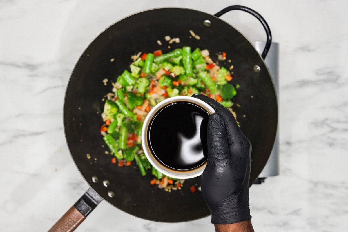 Soy sauce in a bowl over wok with vegetables