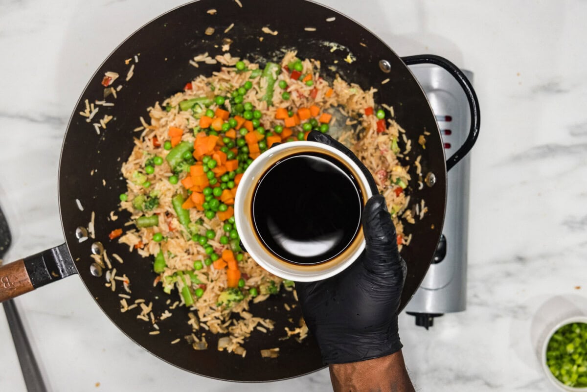 adding soy sauce to wok with vegetable fried rice