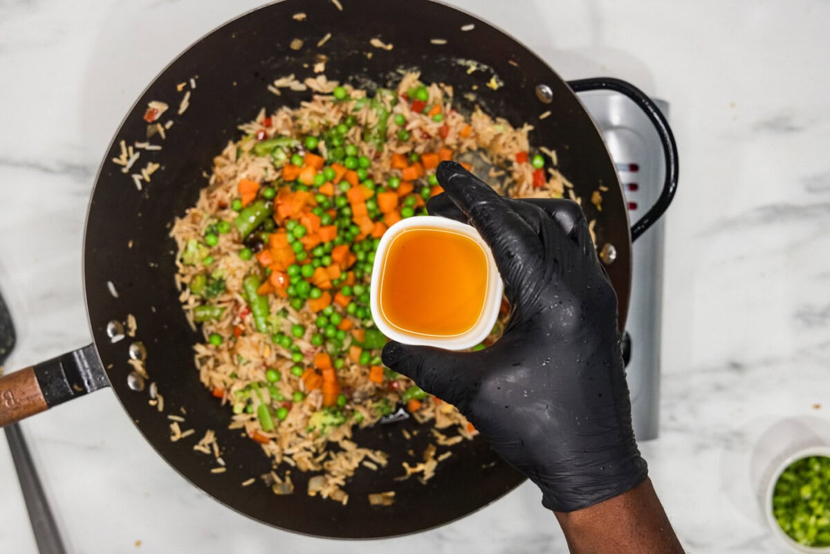 sesame oil in a bowl held over a wok of vegetable fried rice
