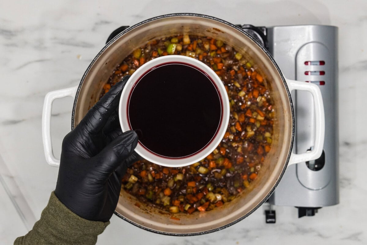 Red wine in a bowl over a dutch oven of vegetables