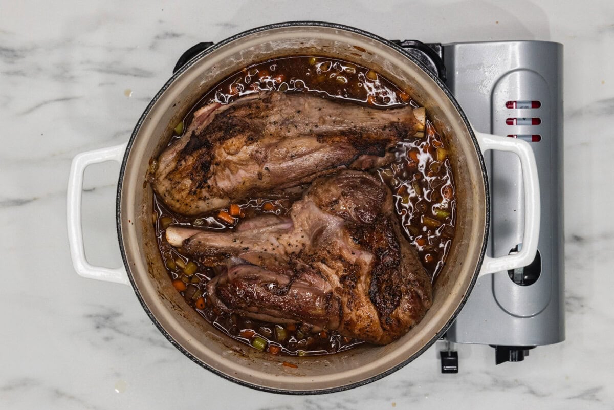 lamb shanks braising in red wine in a dutch oven