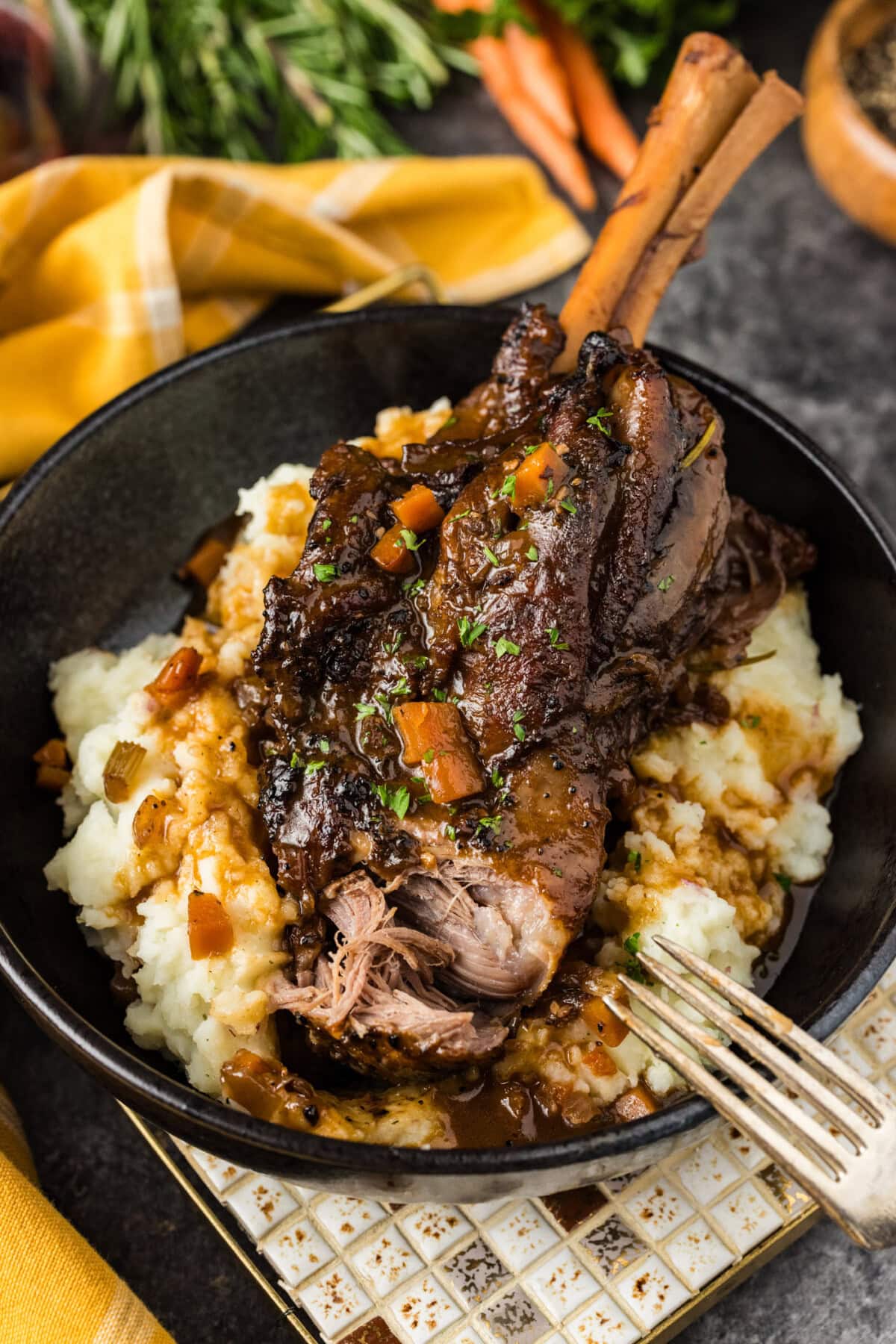 Close up photo of a Braised Lamb Shank served over mashed potatoes with a bite removed