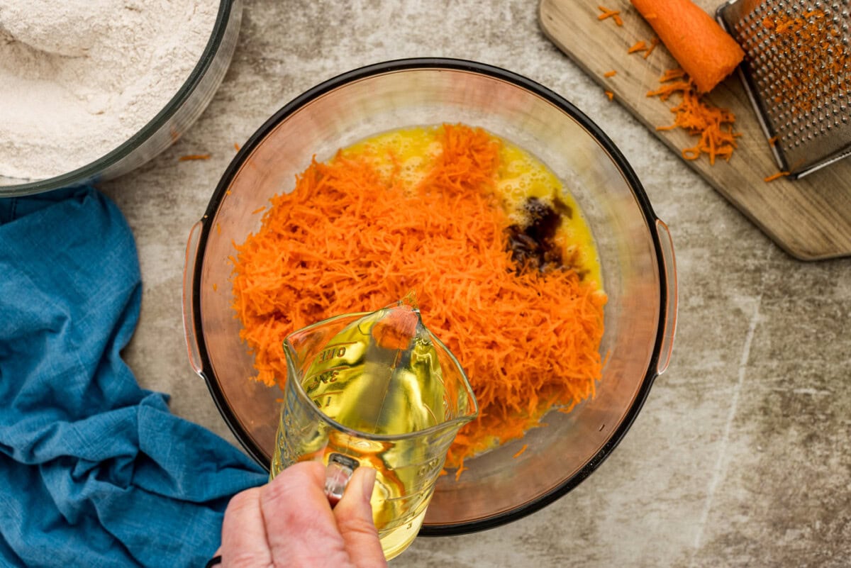 pouring canola oil into bowl of shredded carrots, eggs, and vanilla