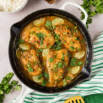 Coconut Chicken in a skillet with rice, herbs and linens on the side
