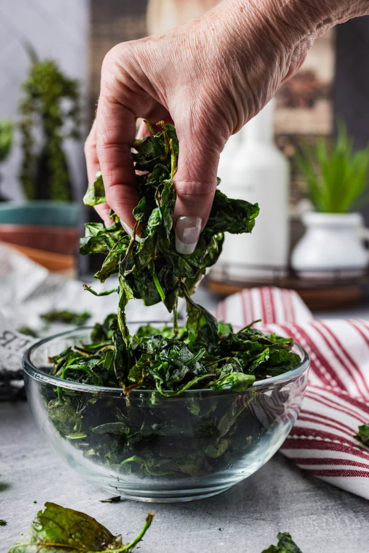 Handful of Crispy Air Fryer Spinach held above a bowl of Crispy Air Fryer Spinach