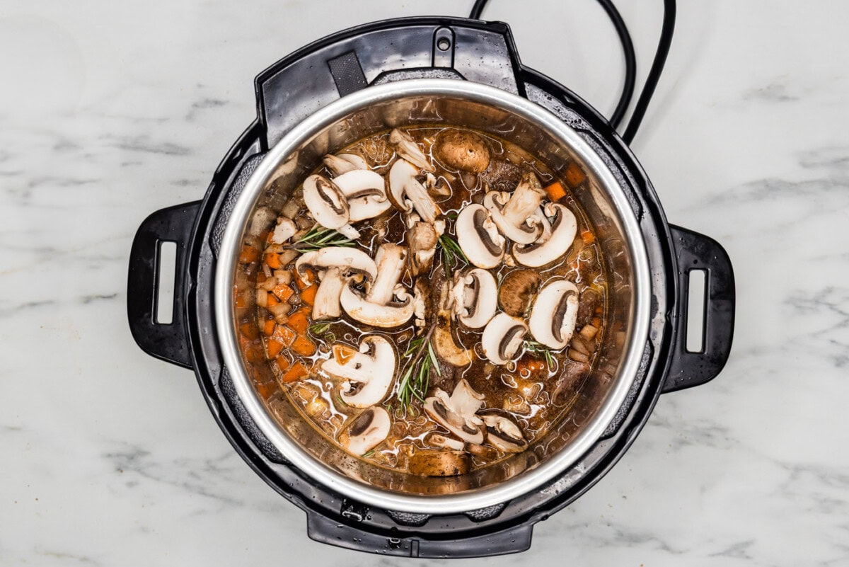 sliced mushrooms and rosemary added to beef shanks in instant pot
