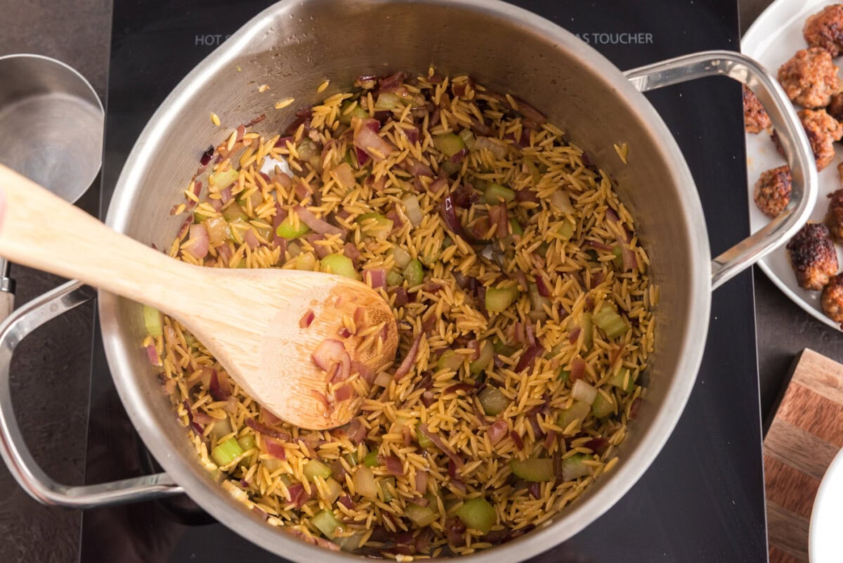wooden spoon in a pot with orzo, sausage, and veggies