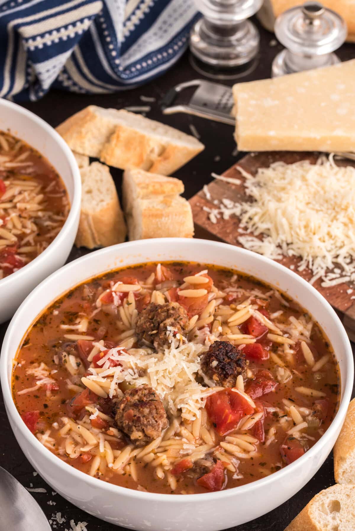 Two bowls of Italian Sausage Tomato Orzo Soup with bread and cheese in the background