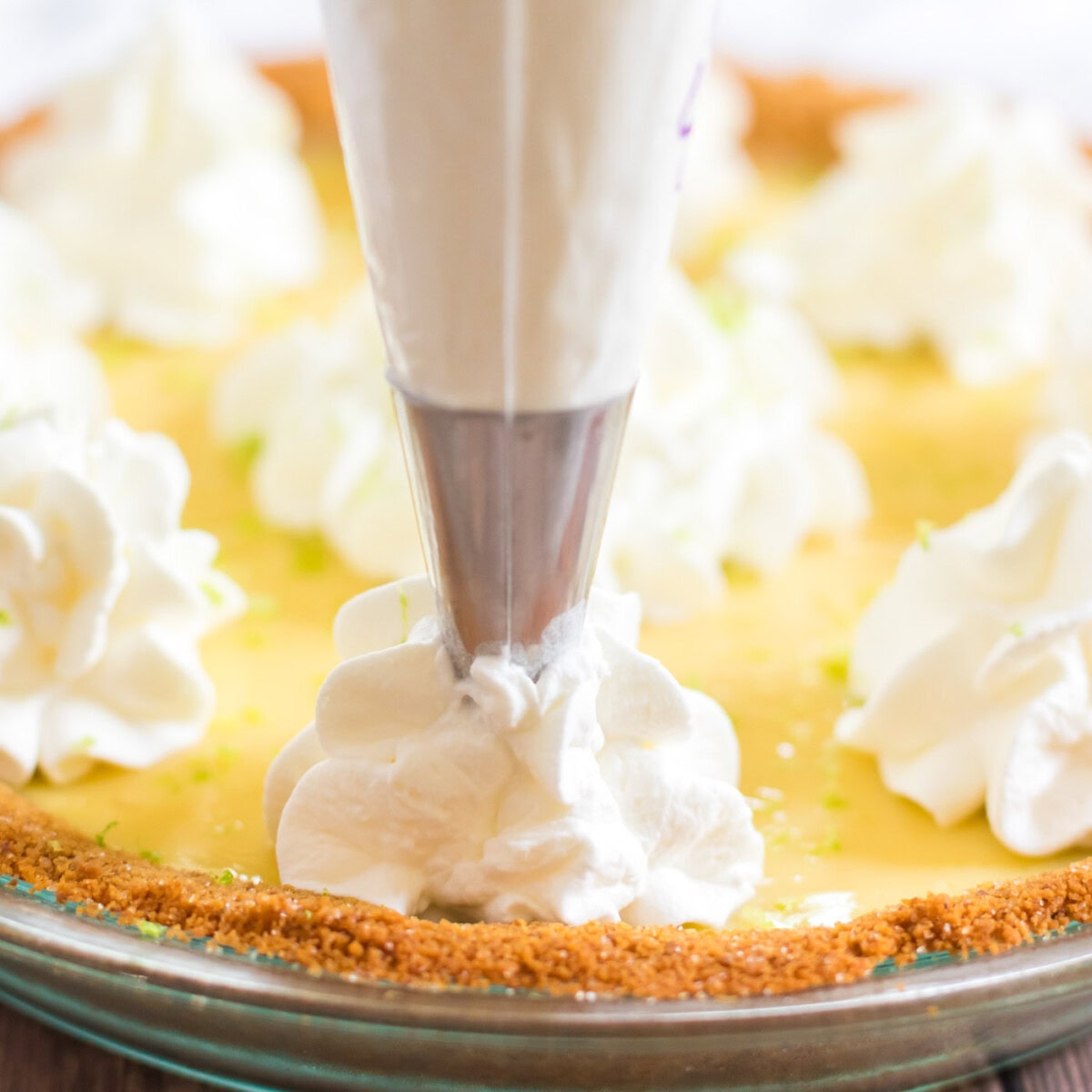 piping whipped cream on to key lime pie