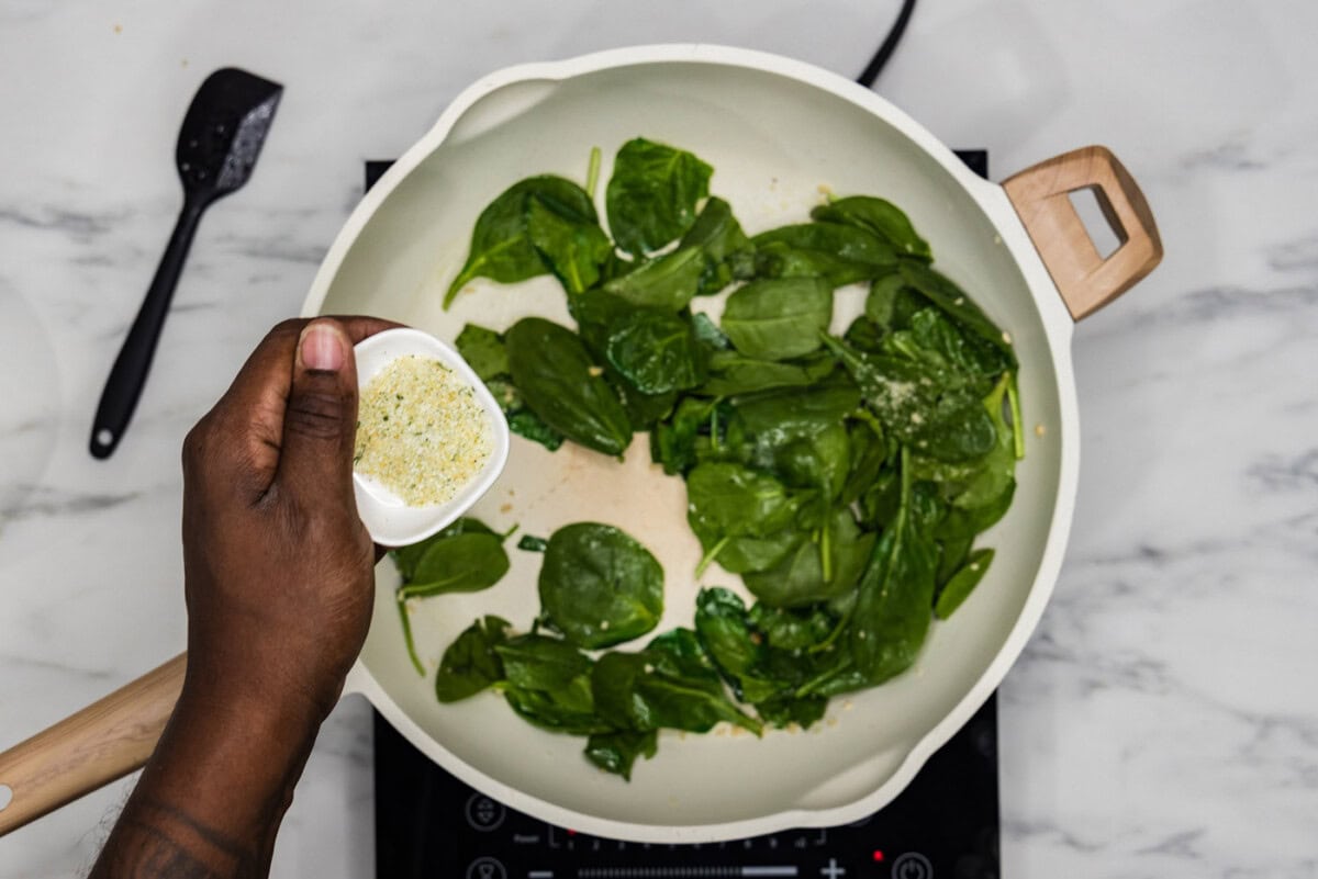 seasoning spinach in a skillet with garlic salt
