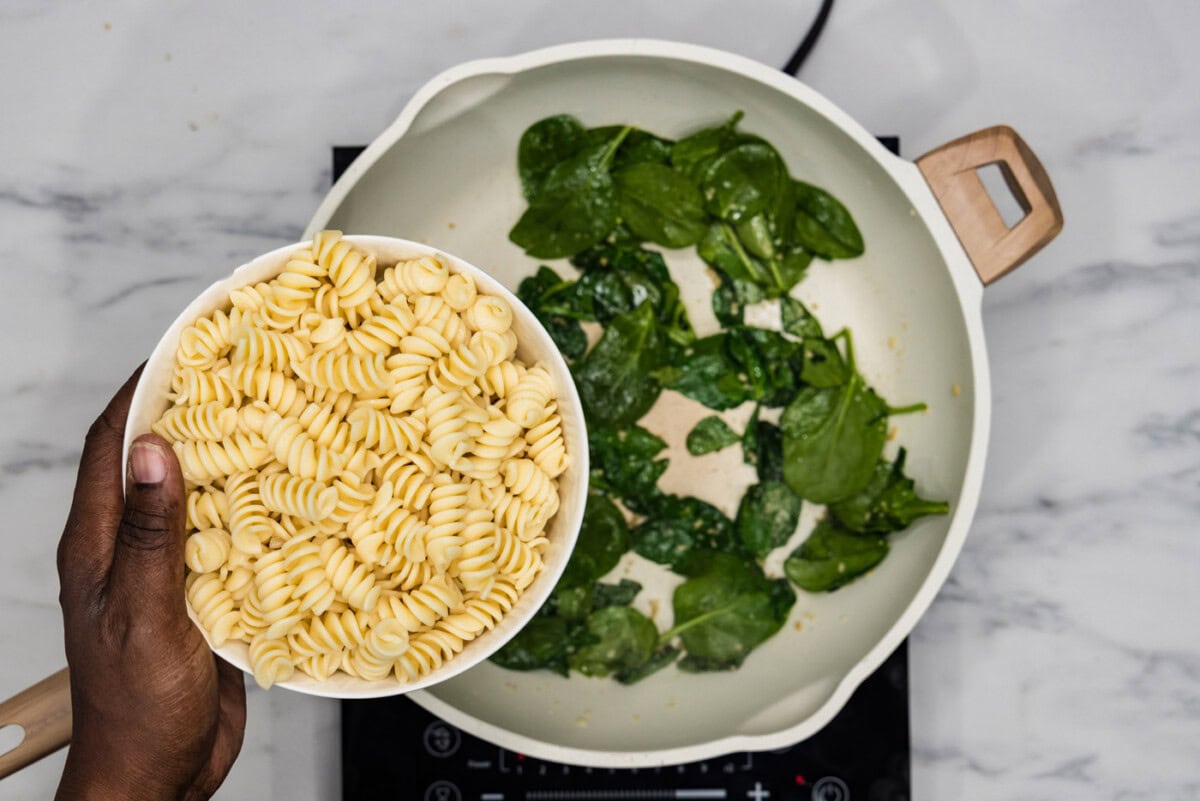 adding pasta to spinach in a skillet