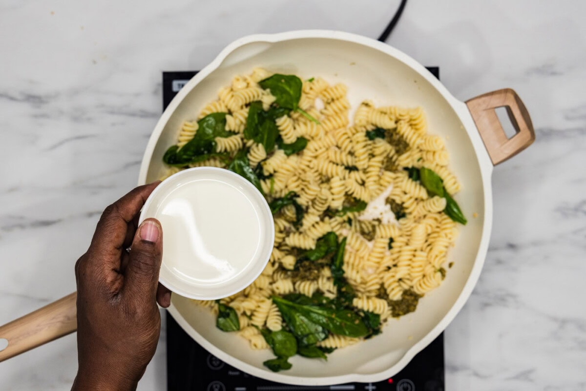 adding heavy cream to skillet with spinach and pasta